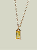 The Lila Necklace by LLUME Jewelry features a gold-plated chain and a rectangular yellow gemstone pendant in a minimalist gold frame, shown on a light beige background.