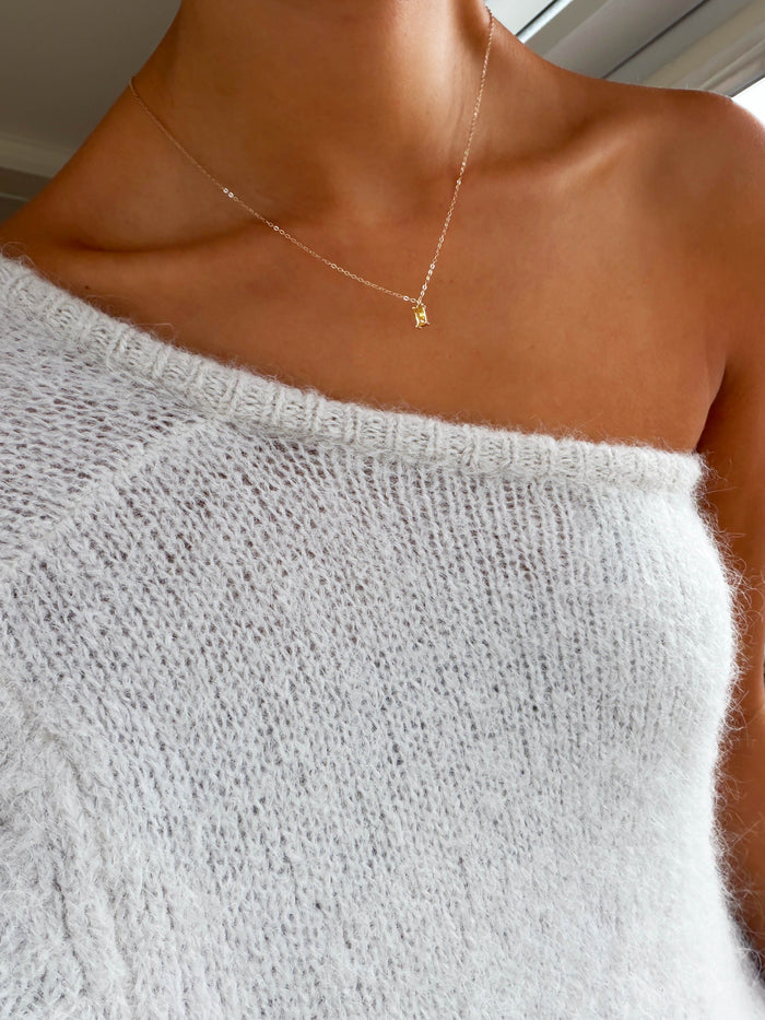 A person wearing a soft white off-the-shoulder sweater and the LLUME Jewelry Lila Necklace, a delicate gold-plated piece with a small pendant, showing bare shoulders and collarbone.