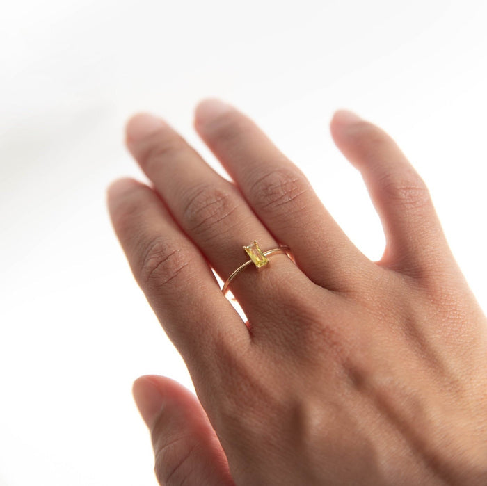 A close-up of a hand wearing the Lila Ring by LLUME Jewelry, featuring a rectangular gemstone set in 14k gold-filled metal, showcased against a soft white background.