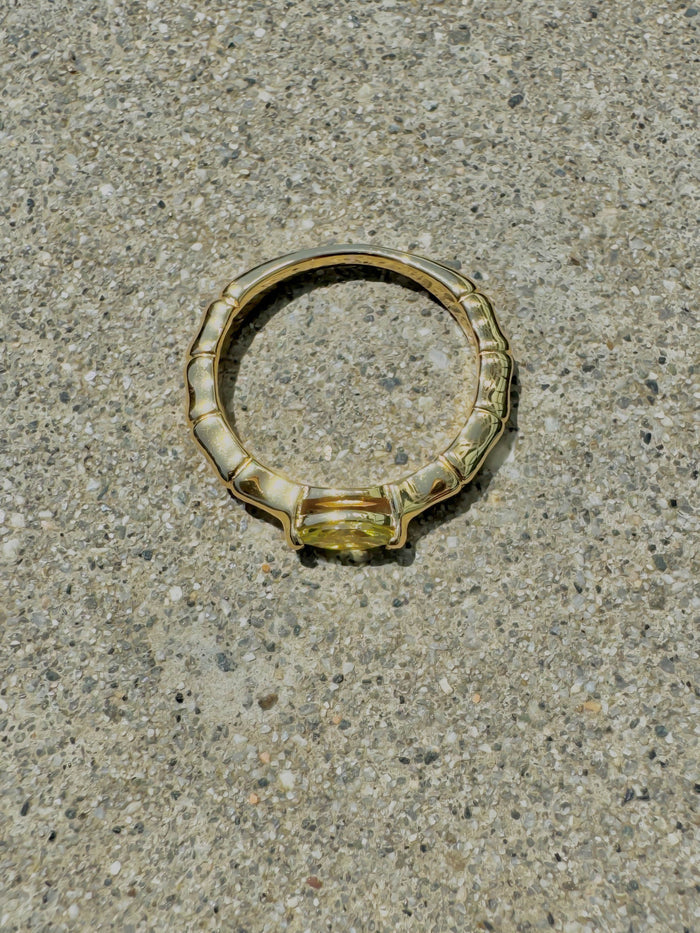 The Limon Ring by LLUME Jewelry, featuring a gold plated 925 sterling silver marquise charm in lemon yellow, rests on speckled concrete and casts a delicate shadow.