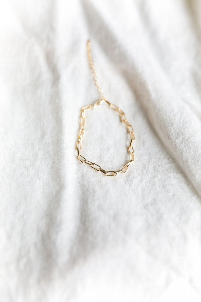 The Link Chain Bracelet by LLUME Jewelry, featuring delicate gold-plated rectangular links, is displayed on a soft white fabric background.