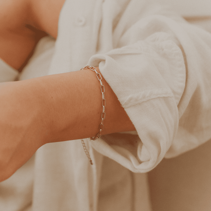 A person in a loose, light-colored long-sleeve shirt with rolled-up sleeves showcases the LLUME Jewelry Link Chain Bracelet on their wrist, set against a softly blurred background for an elegant effect.