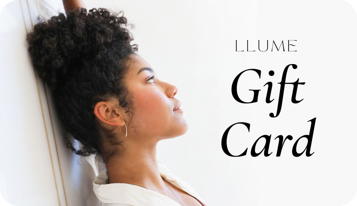 A woman with curly hair leans against a white wall, looking thoughtful. Beside her, text reads: LLUME Jewelry Gift Card—an elegant choice for any occasion, no expiry.