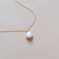 The Lovegood Necklace by LLUME Jewelry is a gold vermeil piece featuring a round white pearl pendant in a minimalist prong setting, shown on a light beige background—a timeless addition to your jewelry collection.
