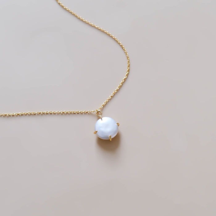 The Lovegood Necklace by LLUME Jewelry is a gold vermeil piece featuring a round white pearl pendant in a minimalist prong setting, shown on a light beige background—a timeless addition to your jewelry collection.