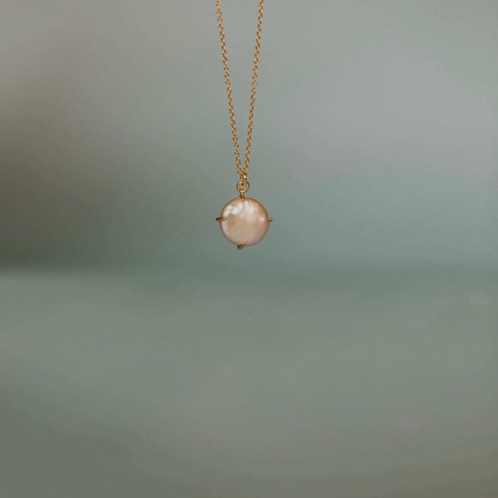 The Lovegood Necklace by LLUME Jewelry features a single round pearl pendant on a gold vermeil chain, elegantly displayed against a soft, blurred green and gray background.