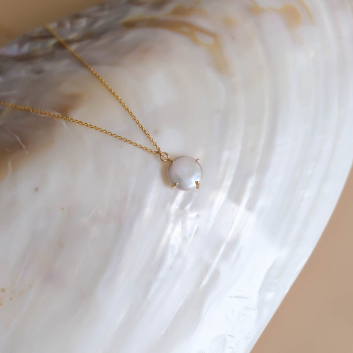 The Lovegood Necklace by LLUME Jewelry, featuring a round pearl pendant on gold vermeil, is displayed on an iridescent shell background, highlighting the timeless elegance of this pearl jewelry piece.