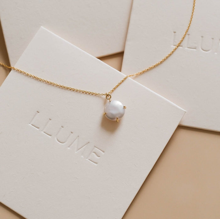 The Lovegood Necklace by LLUME Jewelry, a gold vermeil chain with a single white pearl pendant, is displayed on cream cards embossed with LLUME, highlighting the timeless elegance of pearl jewelry.