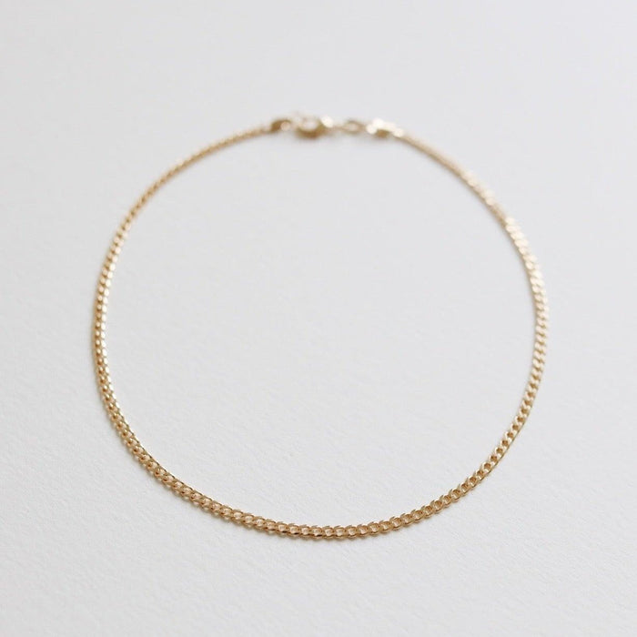 The Marie Chain by LLUME Jewelry is a delicate, thin gold bracelet with a small clasp, shown in a circle on a white background. Perfectly pairs with any 18k gold-filled necklace for an elegant, coordinated style.