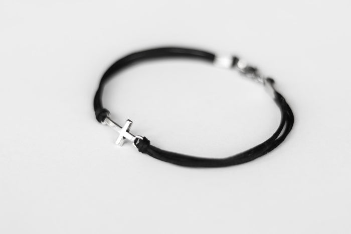 Black string cross bracelet with a silver clasp on a light gray background