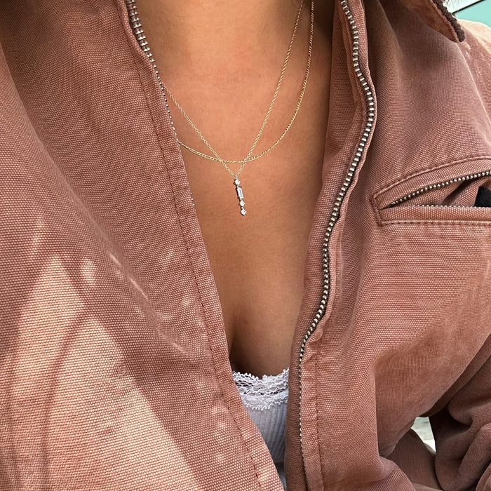 Close-up of a person in a mauve zippered jacket and white lace-trimmed top, wearing the LLUME Jewelry Midnight Daily Set—featuring delicate silver pendants—around their neck.