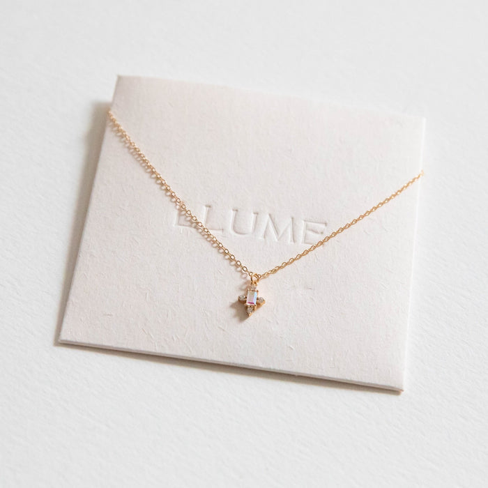 The Moment Necklace by LLUME Jewelry is a dainty gold necklace with a small, rectangular gemstone pendant displayed on a white card embossed with LLUME—a perfect choice for lovers of subtle, color-changing jewelry.