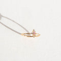 The Moment Ring by LLUME Jewelry features a 14k gold-filled band with a central rectangular pink gemstone and two small clear stones, elegantly displayed on a white surface with a soft shadow.