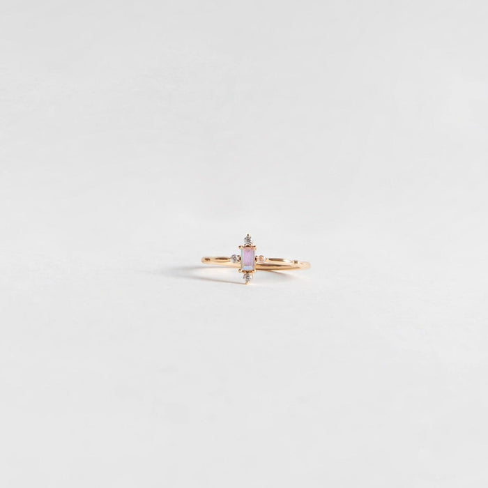 The Moment Ring by LLUME Jewelry features a vertical rectangular pink stone set in 14k gold-filled band, accented with small clear stones, and is displayed on a plain light gray background.