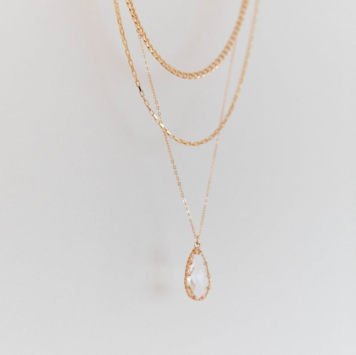 LLUME Jewelry’s New Era Bundle features three delicate gold layered necklaces, one with a clear teardrop gemstone pendant, displayed against a plain light background—an ideal choice to elevate your winter wardrobe.