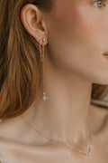 A close-up of a woman’s ear and neck features LLUME Jewelry's Night Sky Earrings—beautiful gold pieces with crescent moon and star details—layered elegantly, ideal for winter style.
