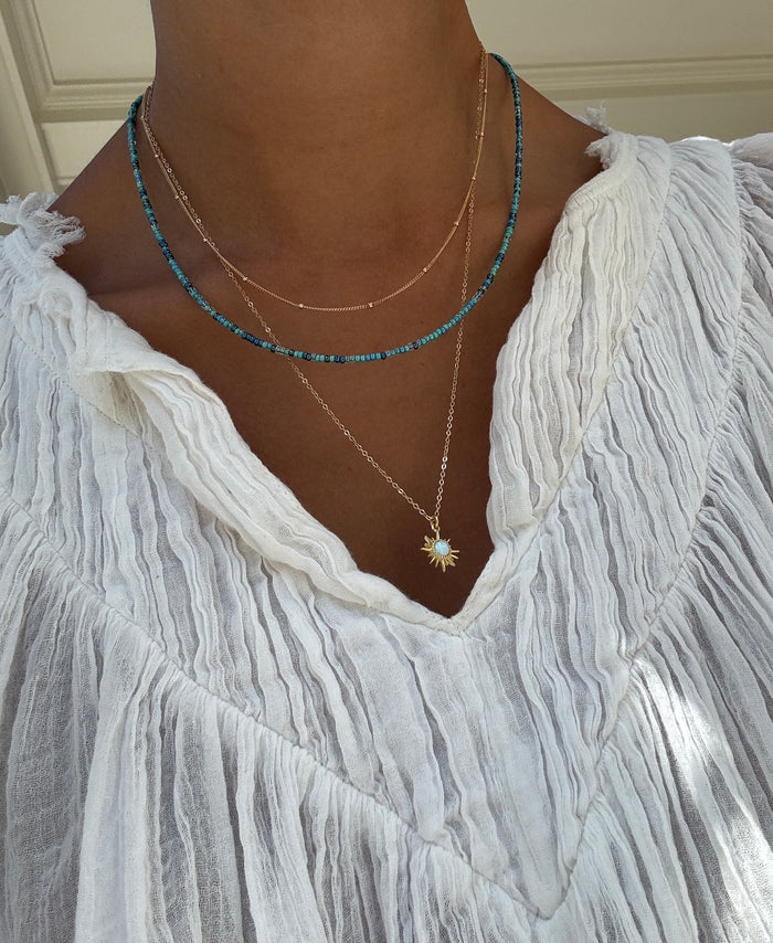 A person wearing a textured white blouse and the Olandria Set by LLUME Jewelry—a chic combo of fine gold chain, blue beaded strand, and gold star pendant—perfect to elevate any jewelry collection with versatile style.