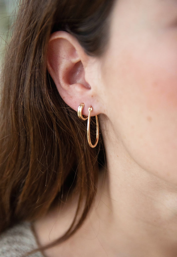 Close-up of a woman's ear with long brown hair, wearing the LLUME Jewelry On my Way Stack—one small gold hoop higher on the ear and one large hoop hanging from the earlobe.