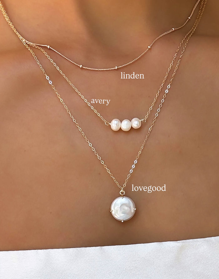 A close-up of a person’s neck wearing LLUME Jewelry’s Pearl Drop Set: a versatile layered necklace set featuring simple and pearl-accented chains.