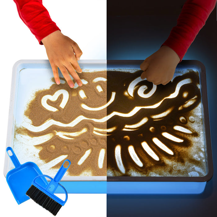 Children's hands playing with sand on a tray, illuminated by a light source.