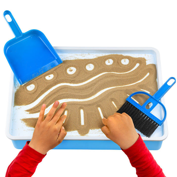 Children's hands playing with sand on a tray with a blue scoop and brush, on a white background