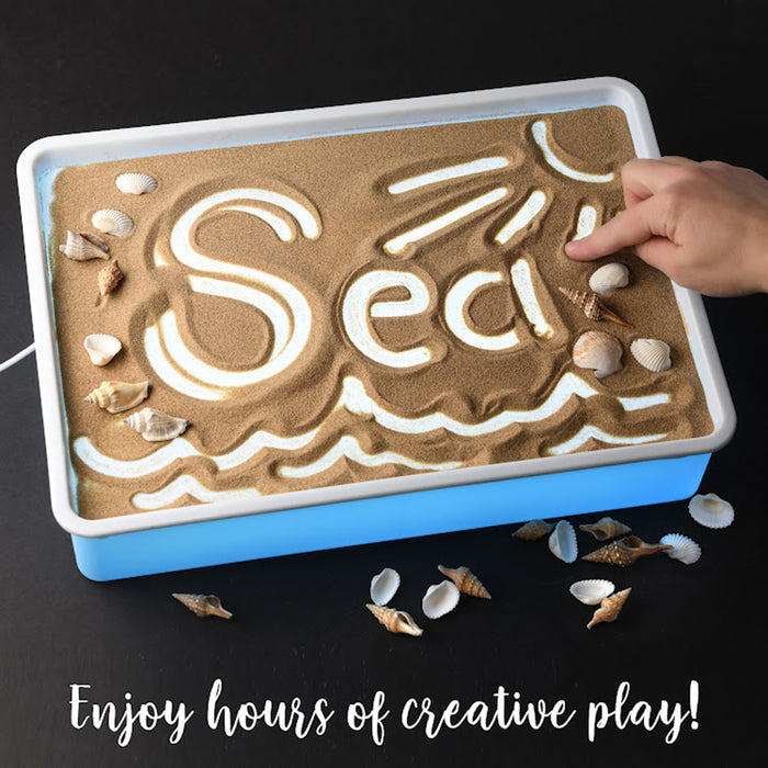 Sand tray with sand art and shells, hand touching the sand, on a black background.