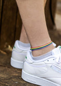 A close-up image of a person's ankle wearing a rainbow-colored cord anklet.