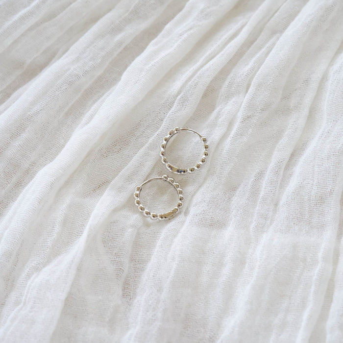 LLUME Jewelry’s Prosecco Beaded Hoops Silver are displayed on a soft, white, textured fabric with gentle folds.