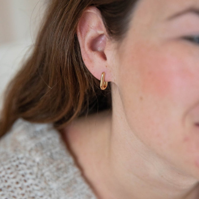 Close-up of a woman with light skin and brown hair wearing LLUME Jewelry’s Rigby Earring—small, tarnish-resistant gold hoops. She is in a textured, light-colored sweater, with only part of her face visible.