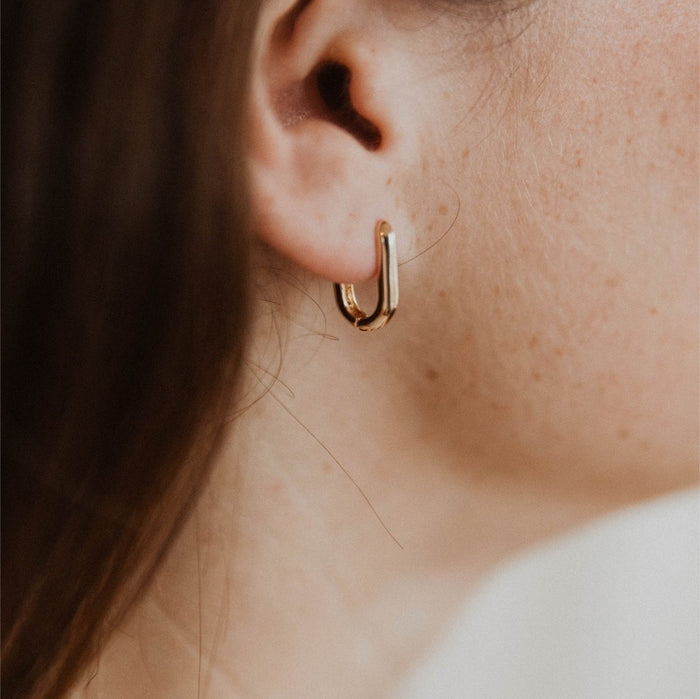 Close-up of a fair, freckled ear wearing LLUME Jewelry's Rigby Earring with gold-filled leverback closure; brown hair frames the face and the softly blurred background keeps focus on the elegant design.