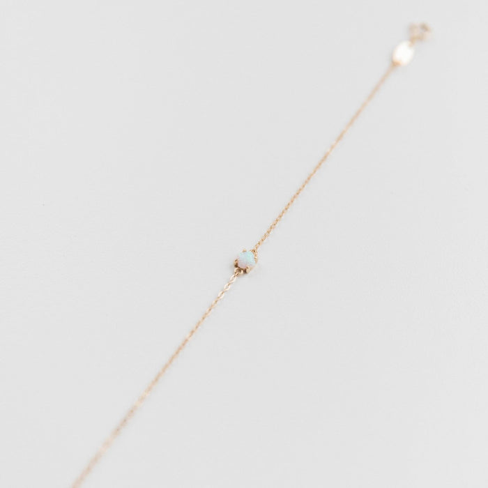 The Sardinia Bracelet by LLUME Jewelry is an adjustable, dainty gold-plated sterling silver piece with a small round blue opal gemstone, shown on a plain white background.