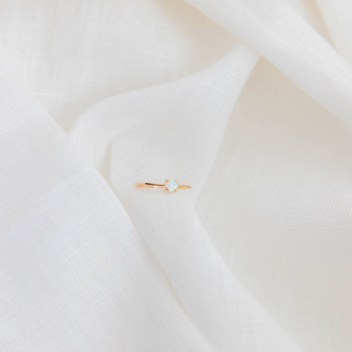 The Sardinia Ring by LLUME Jewelry, a delicate 14k gold filled opal piece, is displayed on softly folded white fabric.