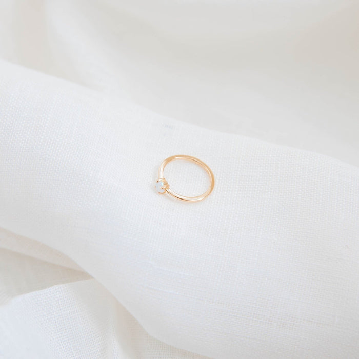 The Sardinia Ring by LLUME Jewelry—a delicate 14k gold filled band set with a single small diamond—is displayed on soft white fabric, highlighting its timeless elegance.
