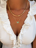 Close-up of someone wearing LLUME Jewelry's Seafoam Favorites Set: a white ruffled top paired with layered necklaces featuring a paperclip chain, skinny hailey chain, and a rectangular seafoam glass pendant.