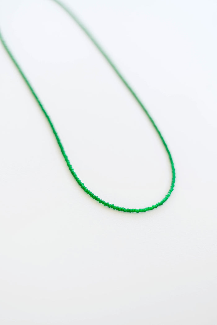 The Searidge Mini Beaded Necklace by LLUME Jewelry features green seed beads, delicately arranged in a loose curve on a simple white background.