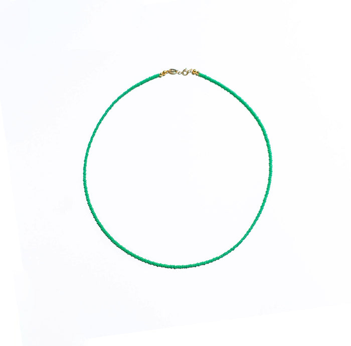 The Searidge Mini Beaded Necklace by LLUME Jewelry features delicate green seed beads and a small gold clasp, showcased in a circular arrangement on a white background.