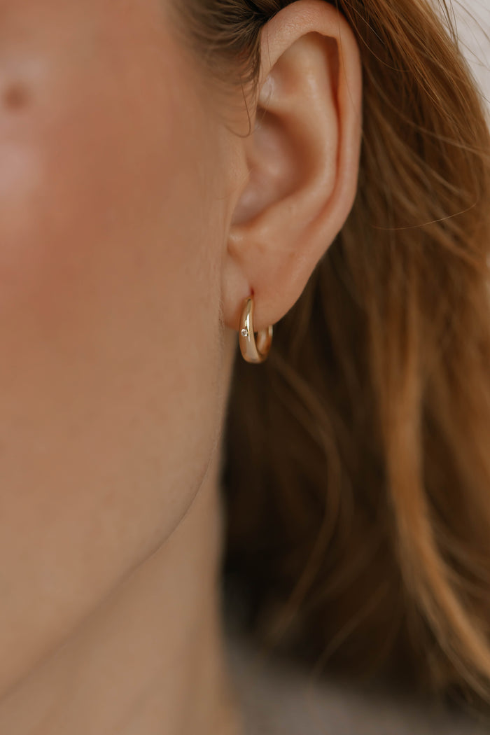 Close-up of a person's ear wearing LLUME Jewelry's Signature Hoops, showcasing timeless gold elegance with part of the cheek and soft-focused brown hair.
