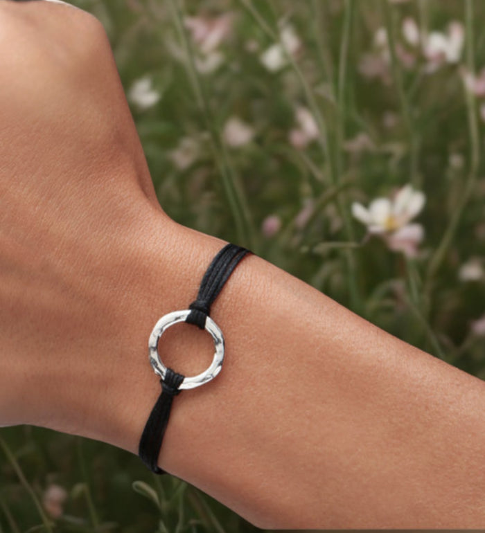 Black bracelet with a silver ring on a wrist against a natural background