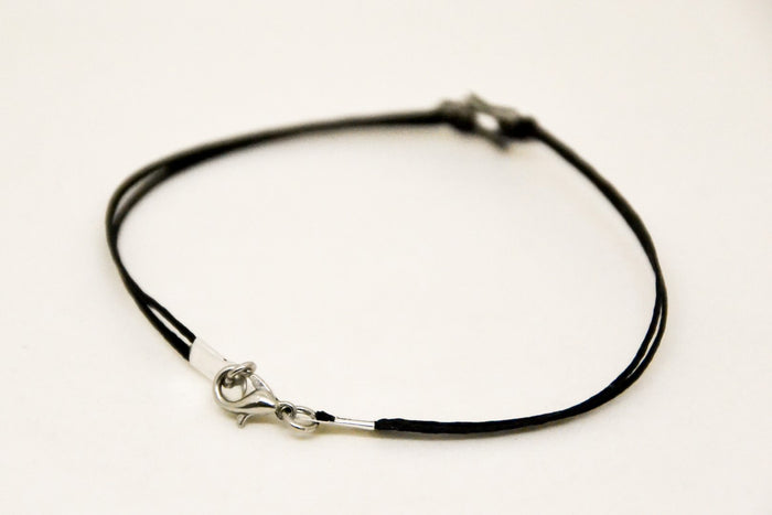 Black leather cord necklace with silver clasp on a light beige background