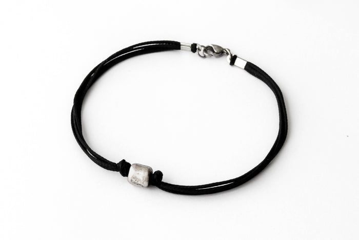 A black cord bracelet for men with a silver tube bead charm and a clasp closure.