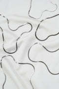 Abstract wavy silver lines on smooth white fabric evoke the elegance of the Skinny Hailey Chain Silver by LLUME Jewelry, with solid 925 silver tones forming organic patterns, soft shadows, and gentle folds in the material.