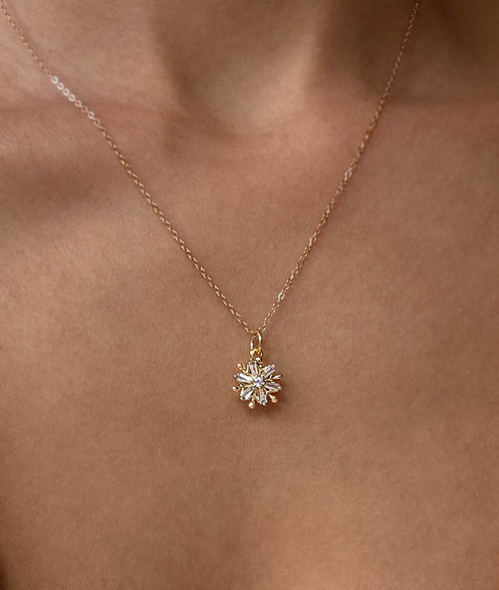 A close-up of the LLUME Jewelry Snowflake Necklace, featuring a gold filled chain and a delicate sunburst pendant with sparkling stones—perfect holiday jewelry, elegantly draped around the neck with bare shoulders.
