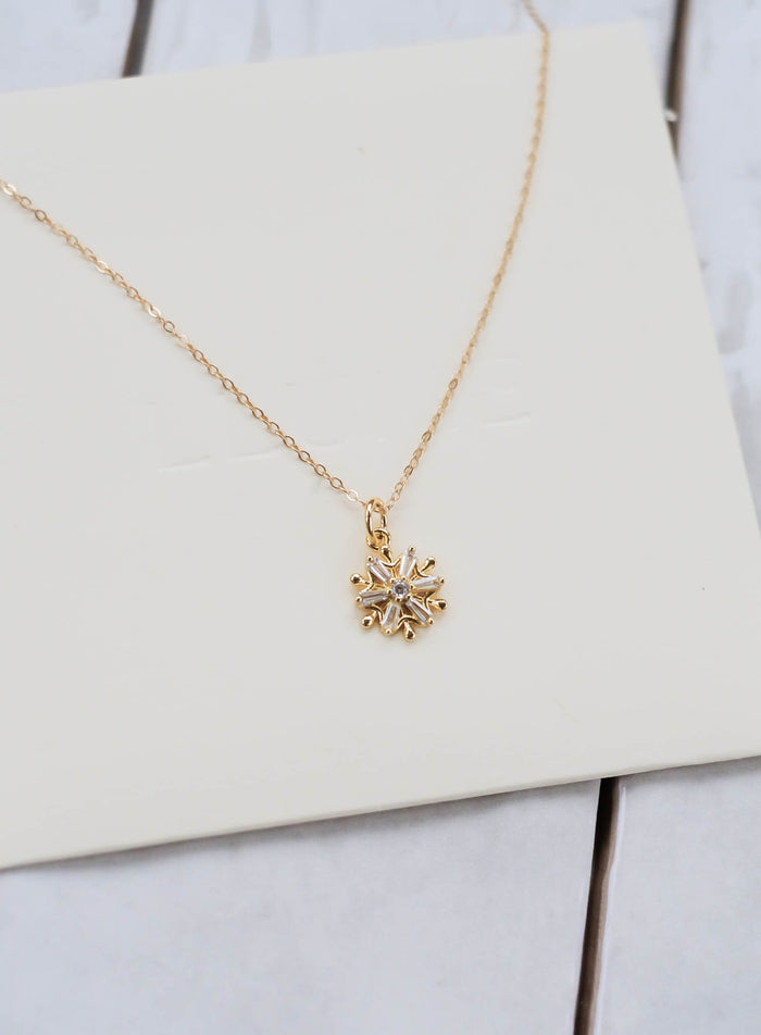 The Snowflake Necklace by LLUME Jewelry features a small, intricate snowflake pendant on a gold filled chain, shown on an off-white background. Ideal as a holiday gift or elegant winter accessory.