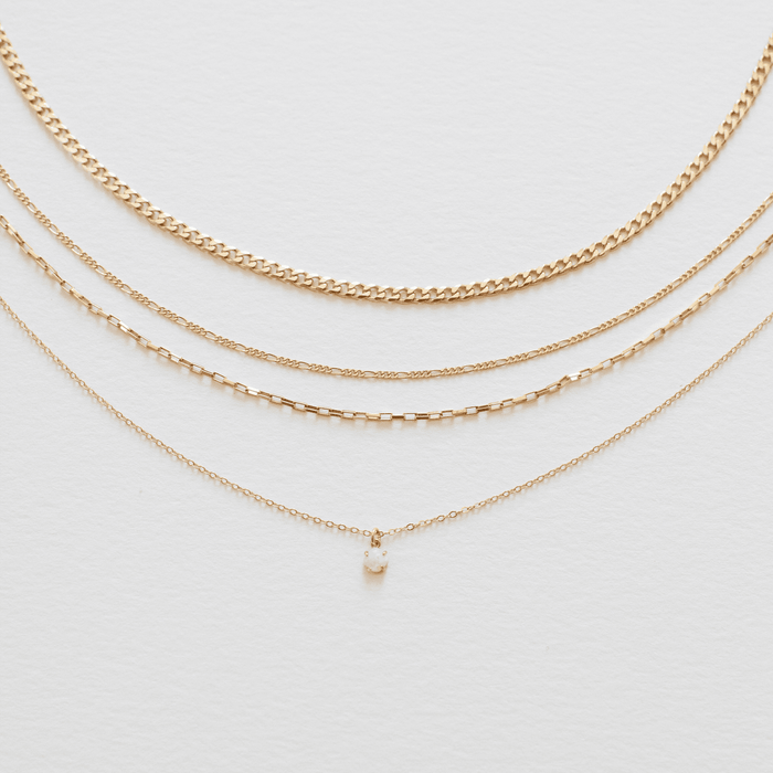 The Solstice Set by LLUME Jewelry features four gold necklaces on a white background; the top three have unique chains and the bottom showcases a dainty opal pendant, creating a chic gold chain bundle.