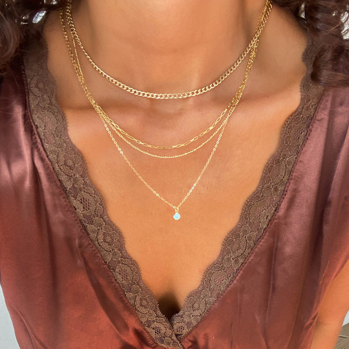 A person wearing a silky, burgundy lace-trimmed top and LLUME Jewelry’s Solstice Set—a gold chain bundle with a dainty opal pendant—shown from shoulders to just above the chest.