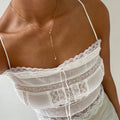 A woman wears a white lace camisole with a drawstring neckline, paired with the elegant Sophia Necklace by LLUME Jewelry—an 18k gold filled long drop piece. The look features intricate lace and is set against a plain light background.