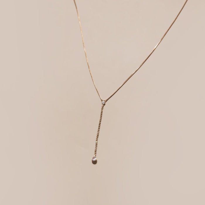 The Sophia Necklace by LLUME Jewelry features a delicate 18k gold filled vertical bar pendant with a small round pearl at the end, displayed against a plain beige background.