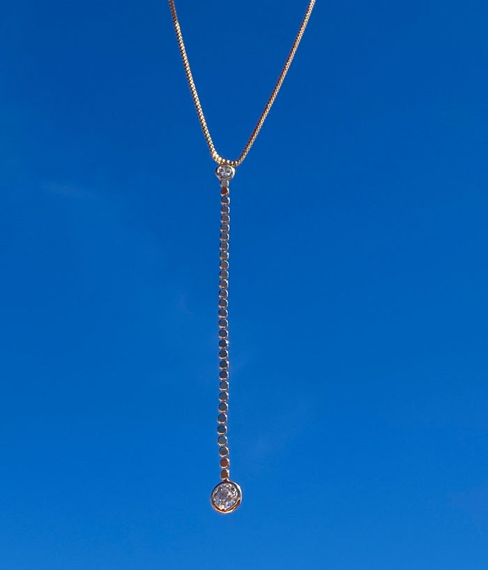 The Sophia Necklace by LLUME Jewelry features a delicate chain and single round pendant. Crafted in 18k gold fill, this elegant piece is showcased against a clear blue sky background, radiating timeless style.