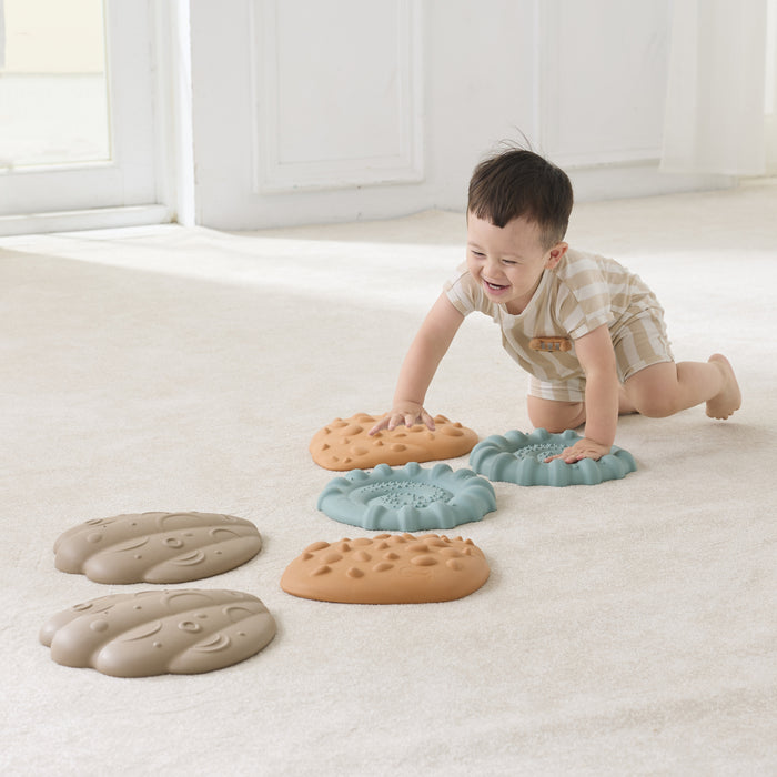 Child playing with colorful tactile shells on a light-colored floor.