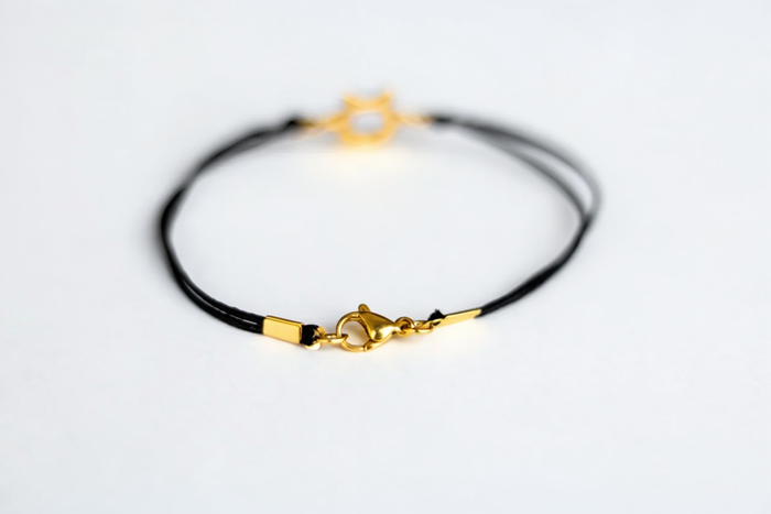 Gold bracelet with black cord on a light gray background